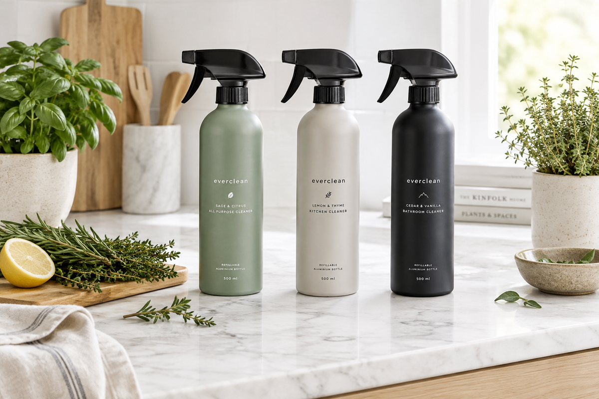 Three refillable aluminium cleaning spray bottles in sage, stone and midnight on a marble kitchen countertop